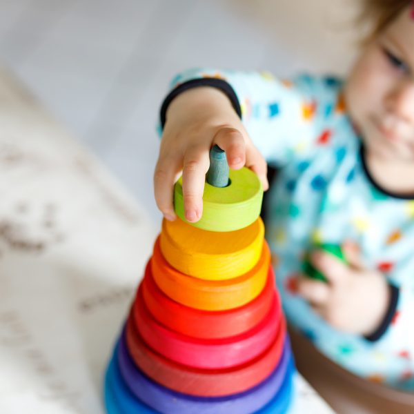 Adorable cute beautiful little baby girl playing with educational toys at home or nursery. Happy healthy child having fun with colorful wooden rainboy toy pyramid. Closeup of hands